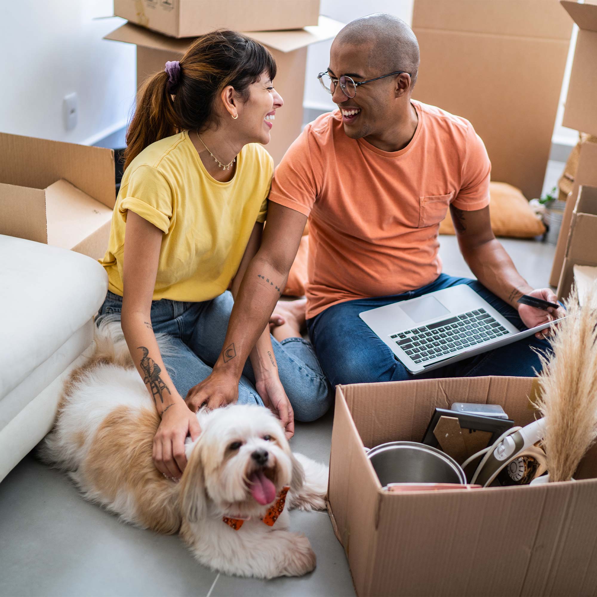 A man and woman along with their dog smile as they unpack.